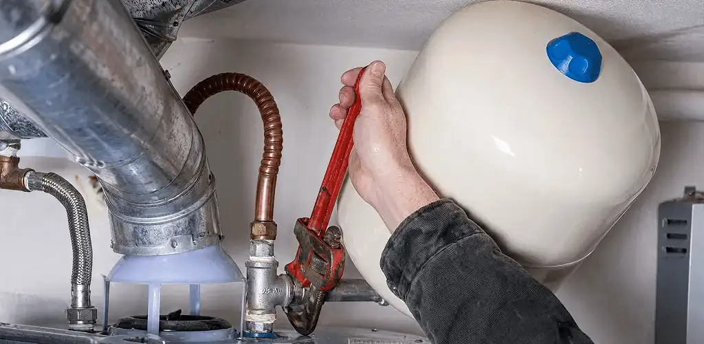Water heater repair technician tightening plumbing connections near a tank unit in St Paul, MN
